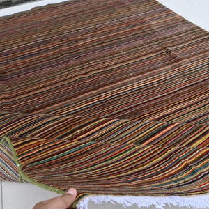 Pode incluir: Um tapete listrado multicolorido com uma borda de franjas. O tapete est&aacute; dobrado ao meio e a franja &eacute; vis&iacute;vel na borda inferior.