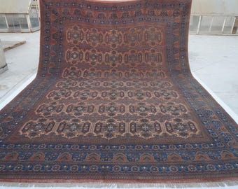 May include: A large rectangular area rug featuring a repeating geometric pattern in shades of terracotta, deep blue, and cream. The rug has a wide decorative border with intricate motifs and a short fringe along the bottom edge of the fabric.