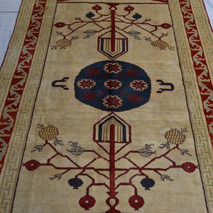 May include: A beige rug with a red, blue, and yellow geometric design. The rug features a central medallion with a stylized tree motif and pomegranate fruit.