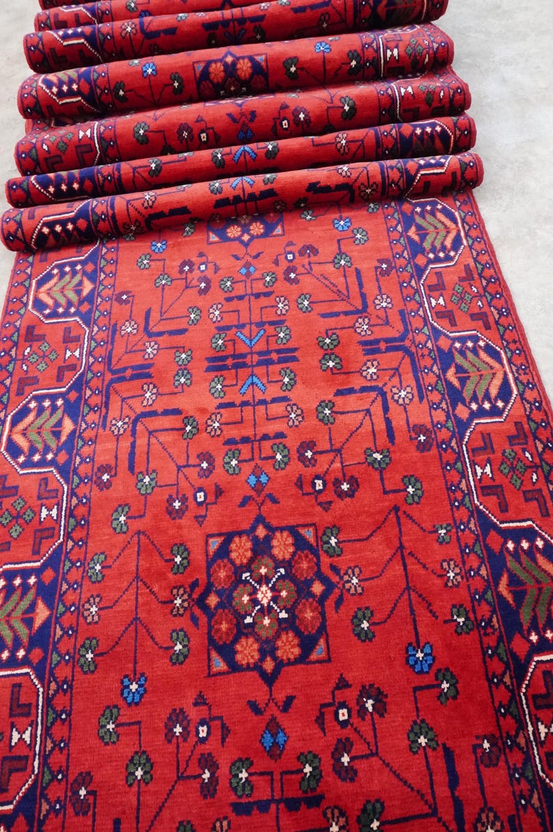May include: A red runner rug with a geometric pattern in shades of blue, green, and brown. The rug has a fringe border and is rolled up.