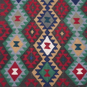 May include: A colorful rug with a geometric pattern in shades of red, blue, green, white, and brown. The pattern is made up of repeating diamond shapes.