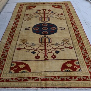 May include: A beige rug with a red and green border. The center of the rug features a stylized tree design with red and blue accents.
