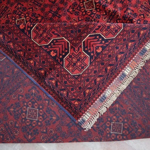 May include: A red and blue rug with a geometric pattern and fringe. The rug is folded in half, showing the back side.