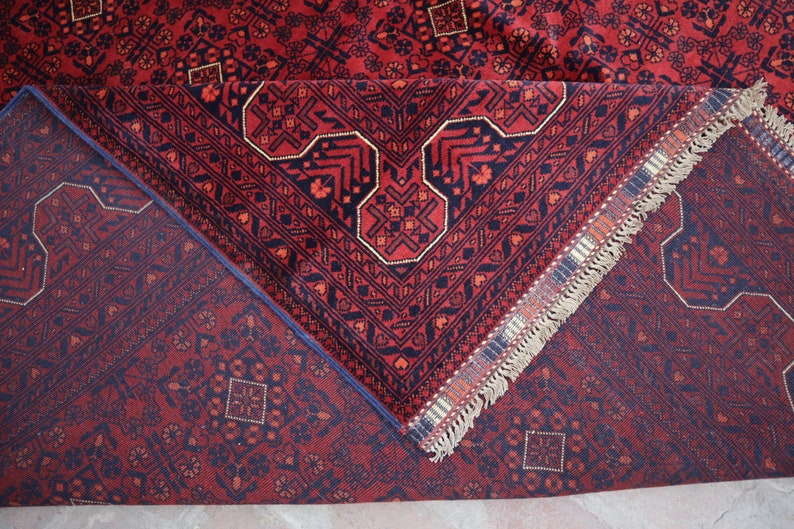 May include: A red and blue rug with a geometric pattern and fringe. The rug is folded in half, showing the back side.