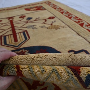 May include: A beige rug with a red, blue, and yellow geometric design. The rug has a fringe border and is folded in half.