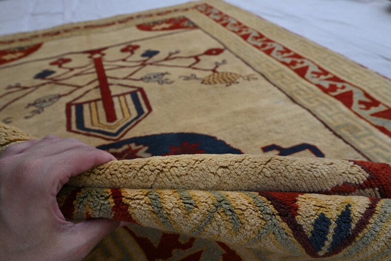 May include: A beige rug with a red, blue, and yellow geometric design. The rug has a fringe border and is folded in half.
