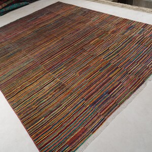 May include: A rectangular area rug featuring a dense, multi-colored striped pattern with thin lines in shades of red, blue, yellow, green, and orange. The rug has a flat-woven texture and includes short, light-colored fringe along the edges.