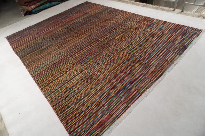 May include: A rectangular area rug featuring a dense, multi-colored striped pattern with thin lines in shades of red, blue, yellow, green, and orange. The rug has a flat-woven texture and includes short, light-colored fringe along the edges.
