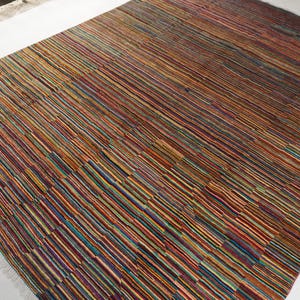 May include: A rectangular area rug featuring a dense pattern of thin, horizontal stripes in a vibrant palette of red, orange, yellow, blue, green, and dark brown. The rug has a flat-woven texture and includes short, light-colored fringe at the edges.