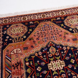 May include: Close-up of a detailed, patterned rug with a central medallion design. The rug features a navy blue border and accents, with a salmon-colored field. Intricate floral and geometric motifs are woven throughout the rug's design.