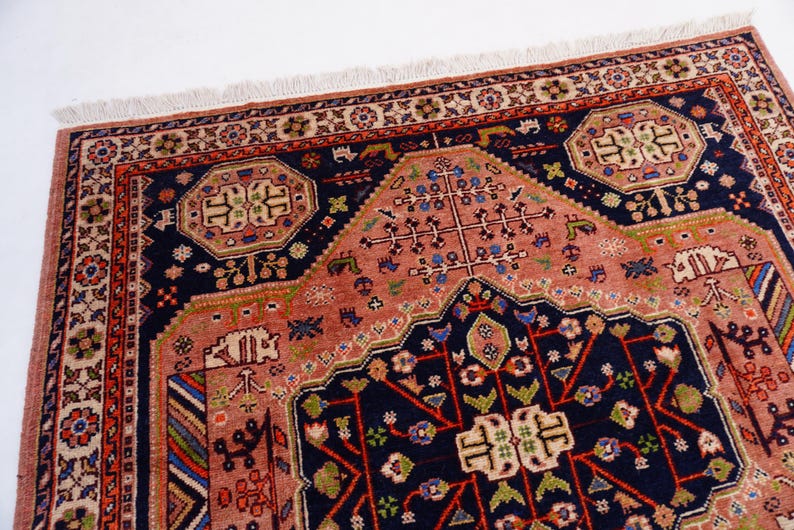 May include: Close-up of a detailed, patterned rug with a central medallion design. The rug features a navy blue border and accents, with a salmon-colored field. Intricate floral and geometric motifs are woven throughout the rug's design.