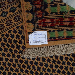 May include: A brown and black patterned rug with a white fringe. The rug has a label that reads "No. 62 - 1595 Size 180 x 114 5-11 x 3-9".