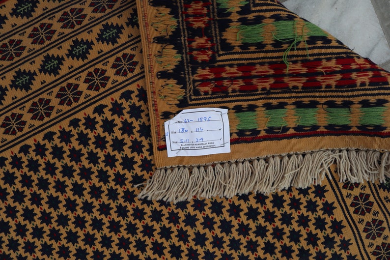 May include: A brown and black patterned rug with a white fringe. The rug has a label that reads "No. 62 - 1595 Size 180 x 114 5-11 x 3-9".