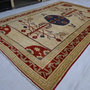 May include: A cream-colored rug with a red, green, and blue geometric pattern. The rug has a fringe border.
