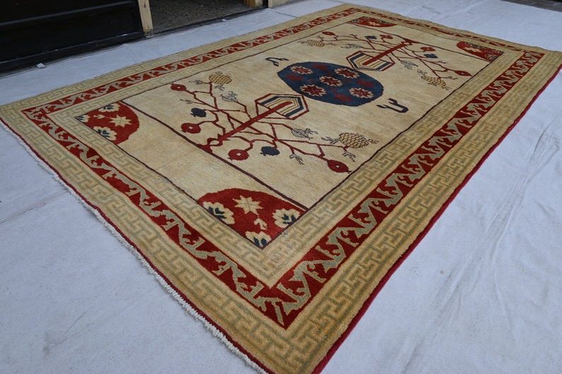 May include: A cream-colored rug with a red, green, and blue geometric pattern. The rug has a fringe border.