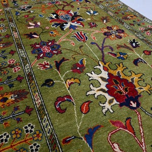 May include: A green rug with a floral pattern in shades of red, blue, yellow, and white. The rug has a border with a geometric design.