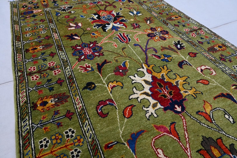 May include: A green rug with a floral pattern in shades of red, blue, yellow, and white. The rug has a border with a geometric design.