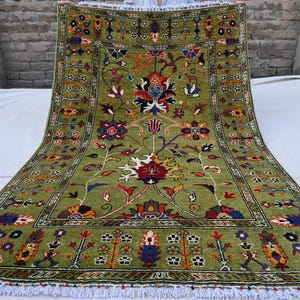 May include: A green rug with a floral pattern in shades of red, blue, and yellow. The rug has a white fringe border.