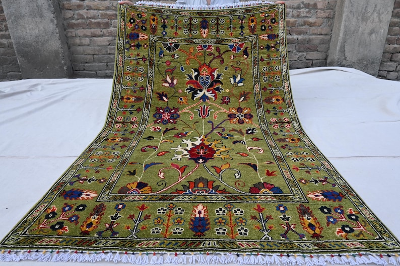 May include: A green rug with a floral pattern in shades of red, blue, and yellow. The rug has a white fringe border.
