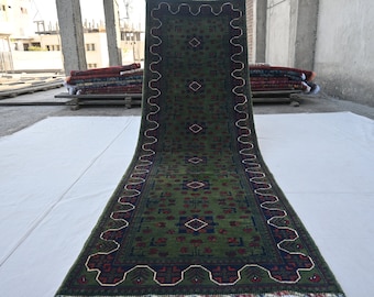 May include: A long green rug with a traditional Persian design. The rug has a dark blue border with a white and red pattern. The rug is folded in half and laid out on a white surface.