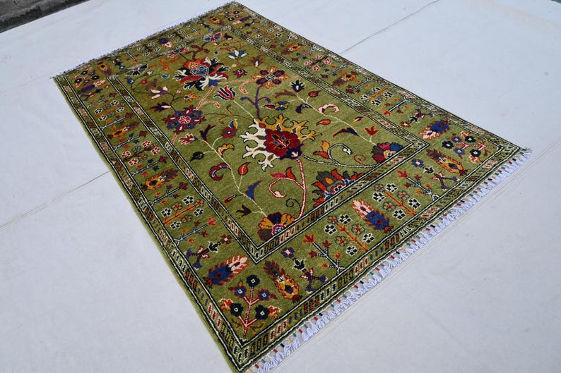 May include: A green rug with a floral pattern in shades of red, blue, and yellow. The rug has a white fringe border.
