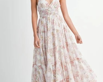 May include: A white maxi dress with a floral print and a tiered skirt. The dress has a V-neckline and thin straps.