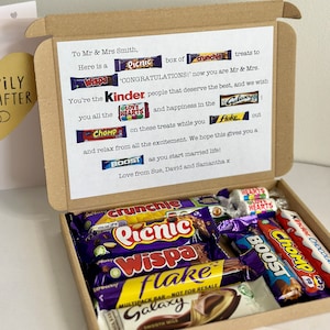 May include: A brown gift box containing a selection of chocolate bars, including Crunchie, Picnic, Wispa, Flake, Galaxy, Boost, and Kinder. The box is decorated with a printed message congratulating the recipients.