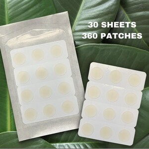 May include: Two packages of round, beige acne patches. One is sealed in a clear plastic pouch, the other is open. The text "30 SHEETS 360 PATCHES" is printed in white on the packaging. The background is green leaves.