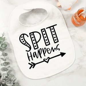 May include: White baby bib with black text that reads "SPIT happens" with a small arrow and heart.