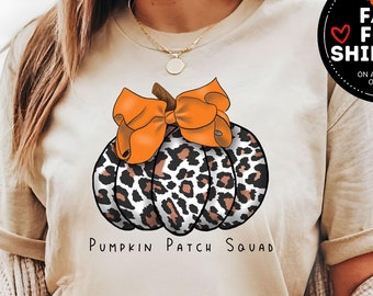 May include: A white t-shirt featuring a brown and black leopard print pumpkin with an orange bow on top. The text "Pumpkin Patch Squad" is printed below the pumpkin.