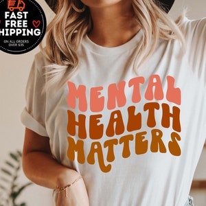 May include: White t-shirt with the text "MENTAL HEALTH MATTERS" in a retro, rainbow-colored font.