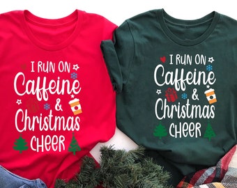 May include: Two red and green t-shirts with a Christmas themed design. The text on the shirts reads "I run on Caffeine & Christmas Cheer".