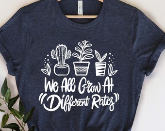 May include: A navy blue t-shirt with a white graphic of potted plants and the text "We All Grow At "Different Rates""