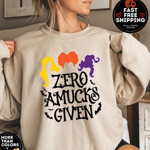 May include: A beige sweatshirt with a black graphic of three witches with the text "Zero Amuks Given".
