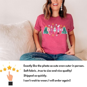 May include: A pink t-shirt with a Christmas-themed design featuring a group of nutcracker characters and a Christmas tree. The design is in a colorful, cartoon style.