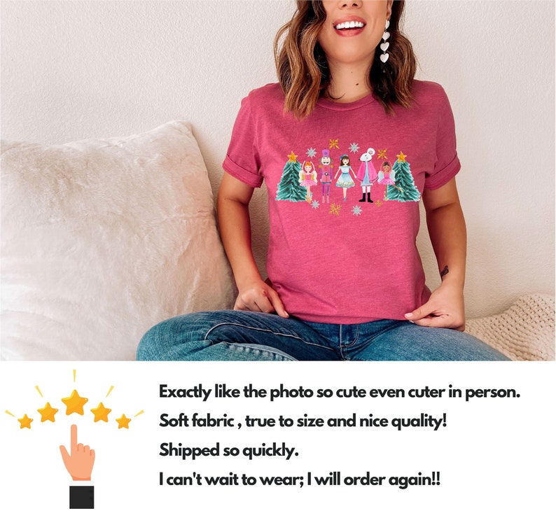 May include: A pink t-shirt with a Christmas-themed design featuring a group of nutcracker characters and a Christmas tree. The design is in a colorful, cartoon style.