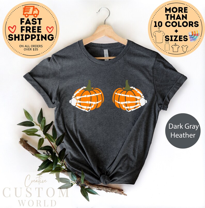 May include: Dark gray heather t-shirt with a graphic of two orange pumpkins with skeleton hands. The pumpkins are positioned as breasts.