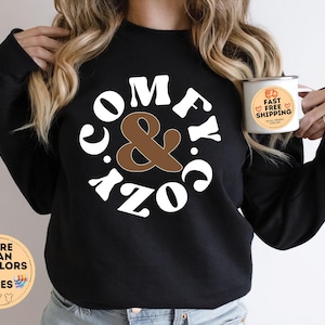 May include: Black sweatshirt with white text that reads "Comfy & Cozy" in a retro font. The text is inside a circle with a brown ampersand in the centre.