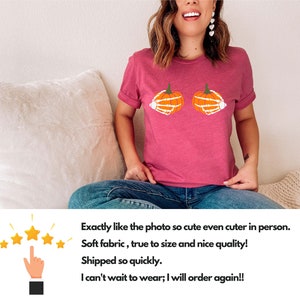 May include: A pink t-shirt with a graphic of two orange pumpkins with white skeleton hands. The pumpkins are positioned as if they are breasts.