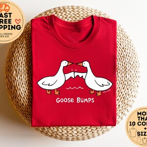 Puede incluir: Camiseta roja con un dise&ntilde;o de piel de gallina blanca. El texto "Goose Bumps" est&aacute; impreso debajo del dise&ntilde;o.