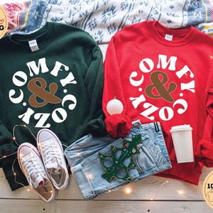May include: Two sweatshirts, one green and one red, with the text "Comfy & Cozy" in a white circle with brown ampersand.
