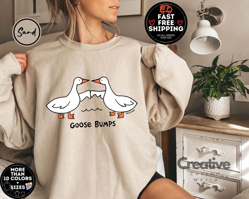 Puede incluir: Una sudadera de color beige claro con un gr&aacute;fico de dos gansos que se miran con el texto "Goose Bumps" impreso debajo.