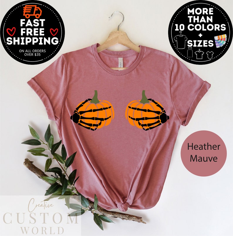 May include: A heather mauve t-shirt with a graphic of two pumpkins with skeleton hands. The text "Creative Custom World" is at the bottom of the image.