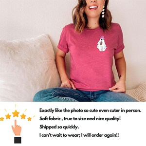 May include: A pink t-shirt with a white ghost wearing a pink hat and holding a cup. The ghost is printed on the front of the shirt.