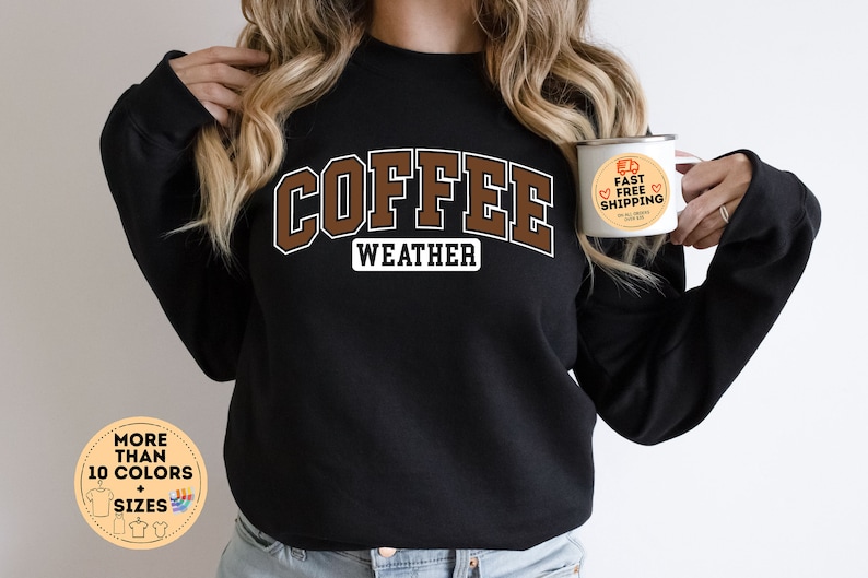 May include: Black sweatshirt with the text "COFFEE WEATHER" in brown letters. The sweatshirt is being modeled by a person holding a white mug with the text "FAST FREE SHIPPING" in orange and red.