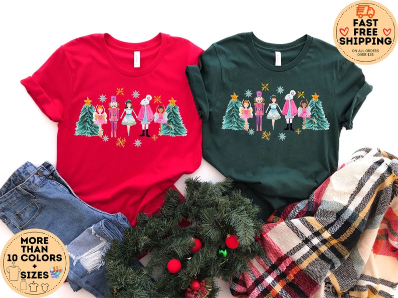 May include: Two red and green t-shirts with a Christmas Nutcracker design. The design features a Nutcracker, a ballerina, a mouse king, and a Christmas tree. The text on the t-shirts says "MORE THAN 10 COLORS + SIZES".