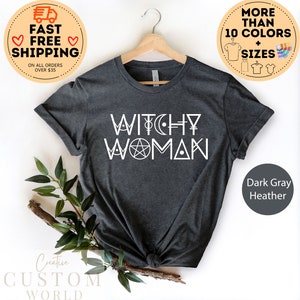 May include: Dark grey heather t-shirt with the text "WITCHY WOMAN" in white. The text is surrounded by various symbols, including a pentagram, a crescent moon, and a female symbol.