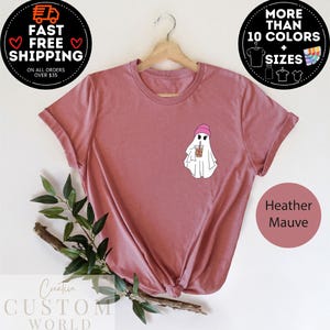 May include: A heather mauve t-shirt with a white ghost wearing a pink beanie and holding a brown iced coffee. The text "Heather Mauve" is printed on the bottom right corner of the image.