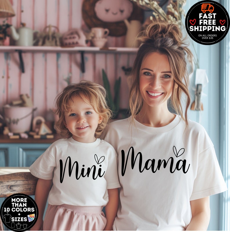 May include: White t-shirts for a parent and child. The adult shirt says "Mama" with a small heart and the child's shirt says "Mini" with a small heart.