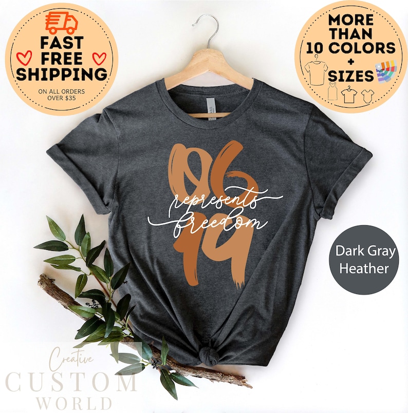 May include: Dark gray heather t-shirt with the text "06 represents freedom 19" in a brown and white design. The shirt is displayed on a wooden hanger. The image also includes text that says "More than 10 colors + sizes".